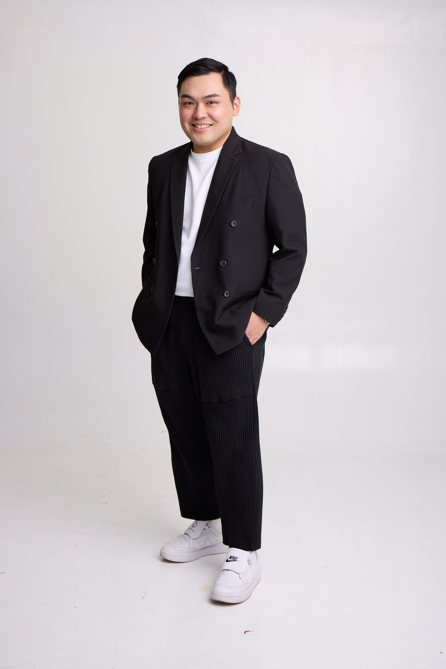 Andrew Sha standing and smiling in a black blazer against a light studio background