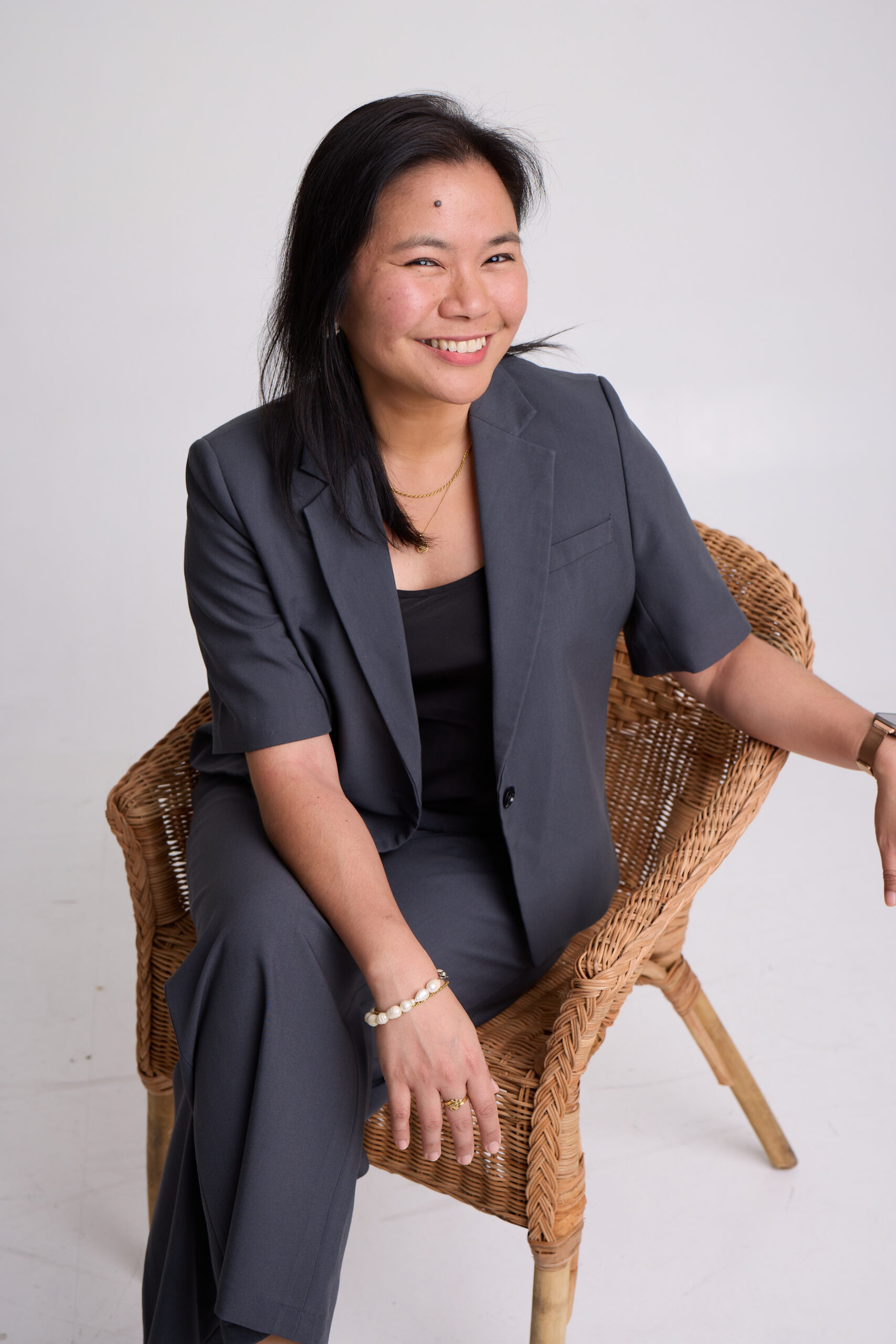 Mich De Guzman seated in a wicker chair wearing a charcoal blazer